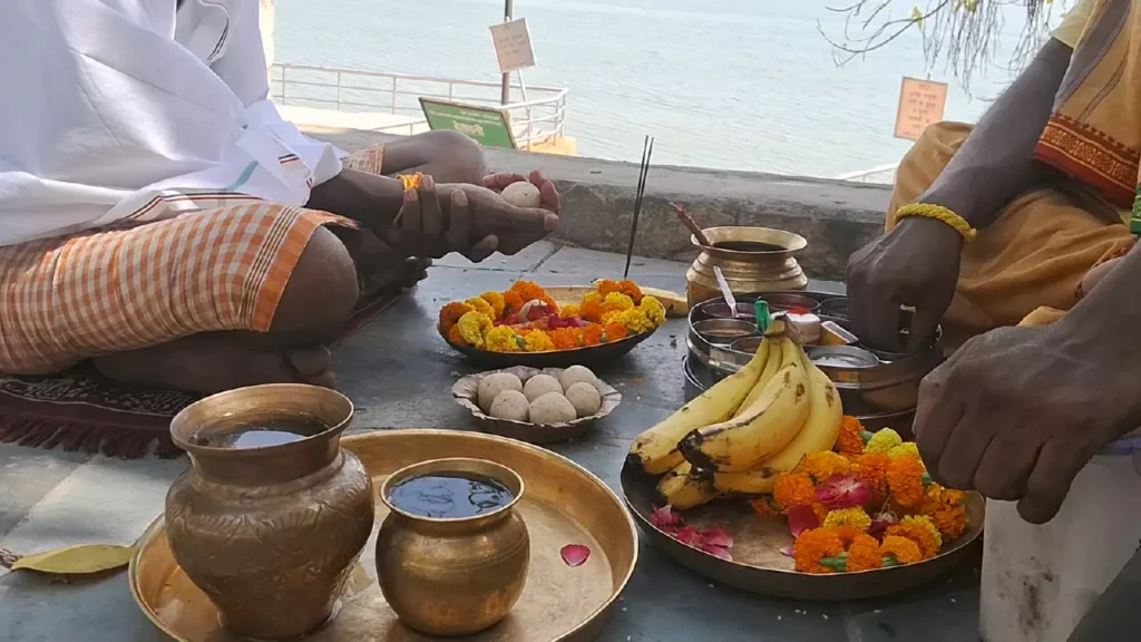 People performing a ritual with offerings like flowers, fruit, and brass pots by the water- Understanding the Ganges Profound Role in Varanasi Asthi Visarjan
