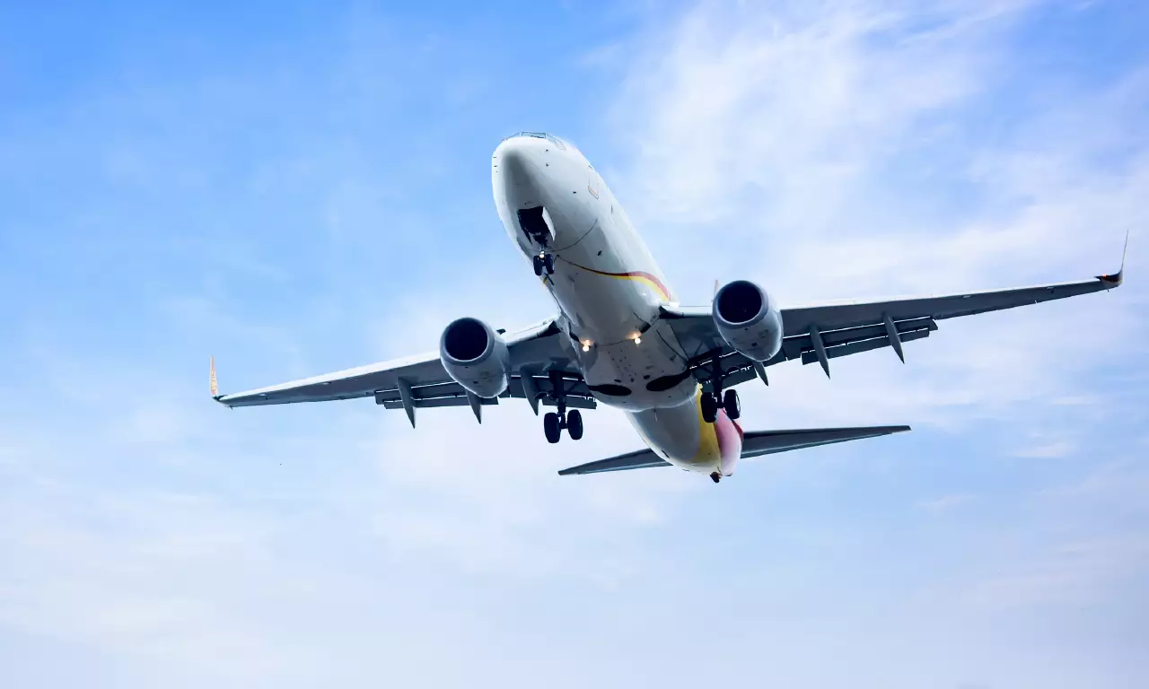 A passenger airplane is seen from below, its landing gear down, as it prepares to land against a blue sky with scattered clouds. Asthi Visarjan in Prayagraj from Singapore.